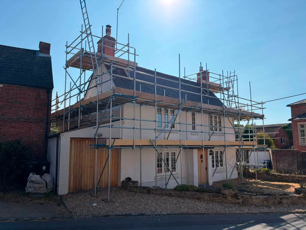 Scaffold around the roofline of a rendered cottage
